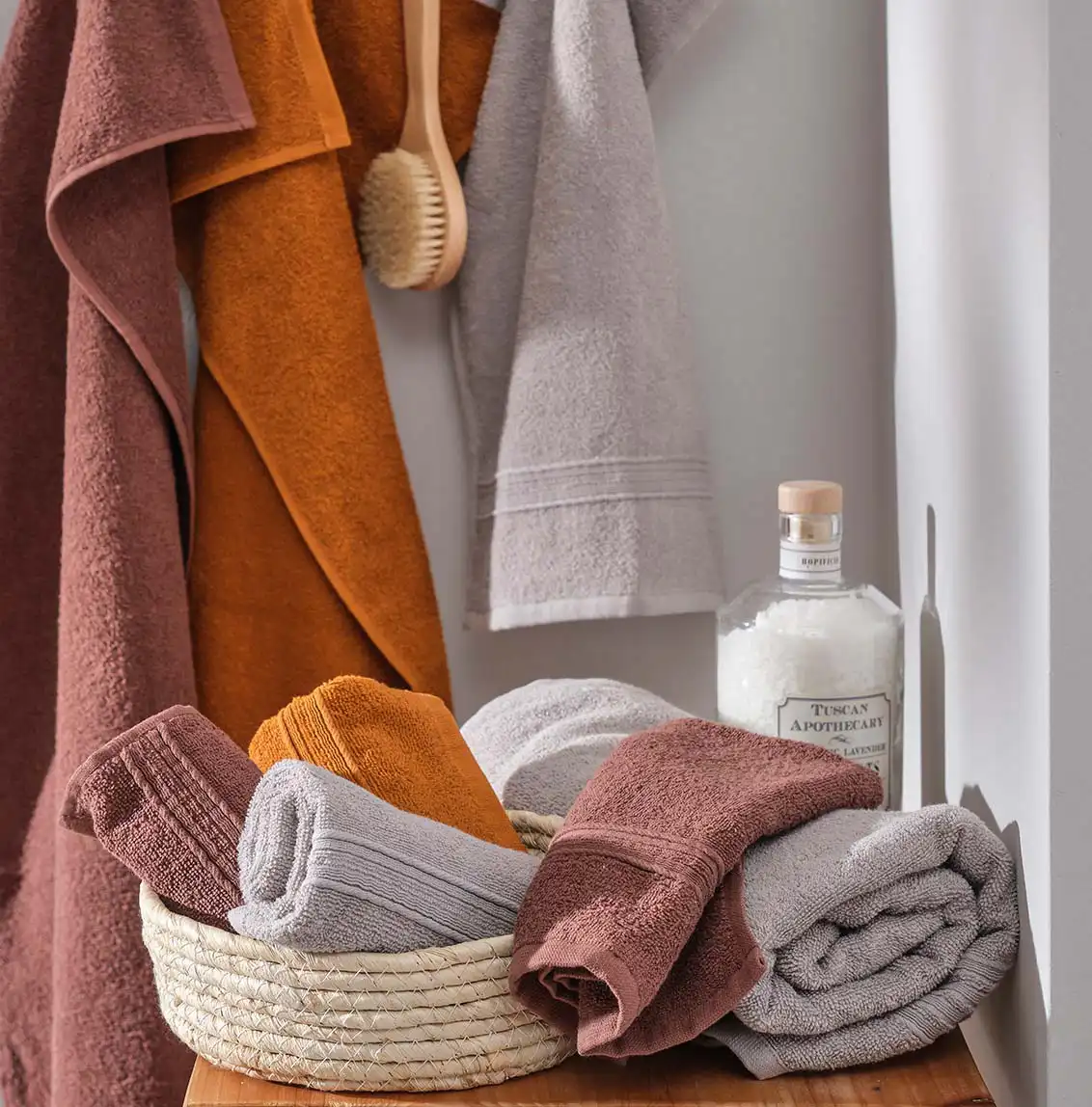 Zachte handdoeken in aardetinten: bruin, okergeel en grijs, hangend aan een houten rekje.