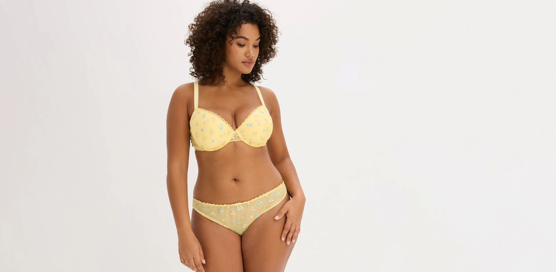 Vrouw die een gele lingerieset met bloemenborduursel draagt.
