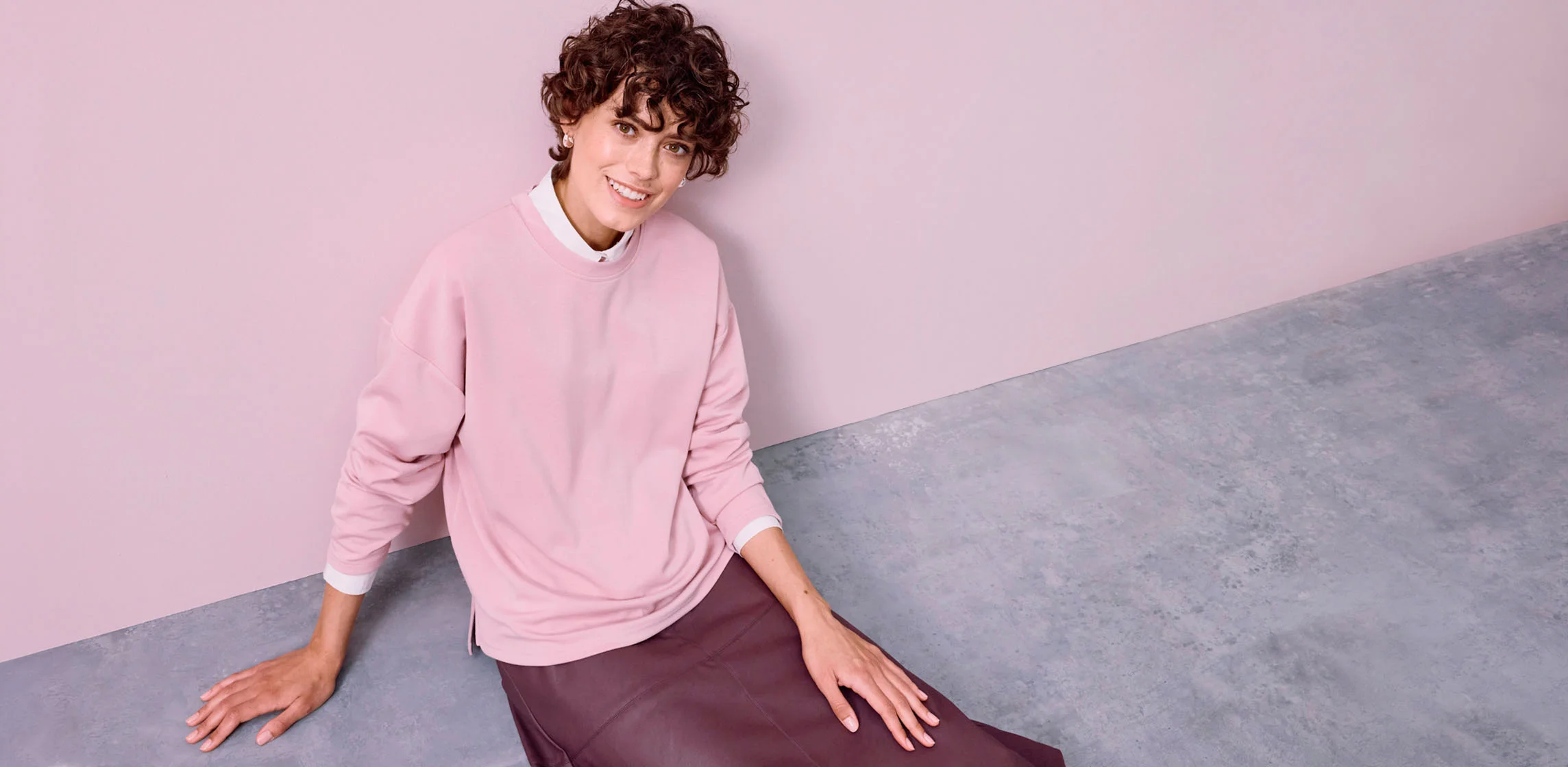 Een losse roze sweater over een wit overhemd, gecombineerd met een donkere rok.