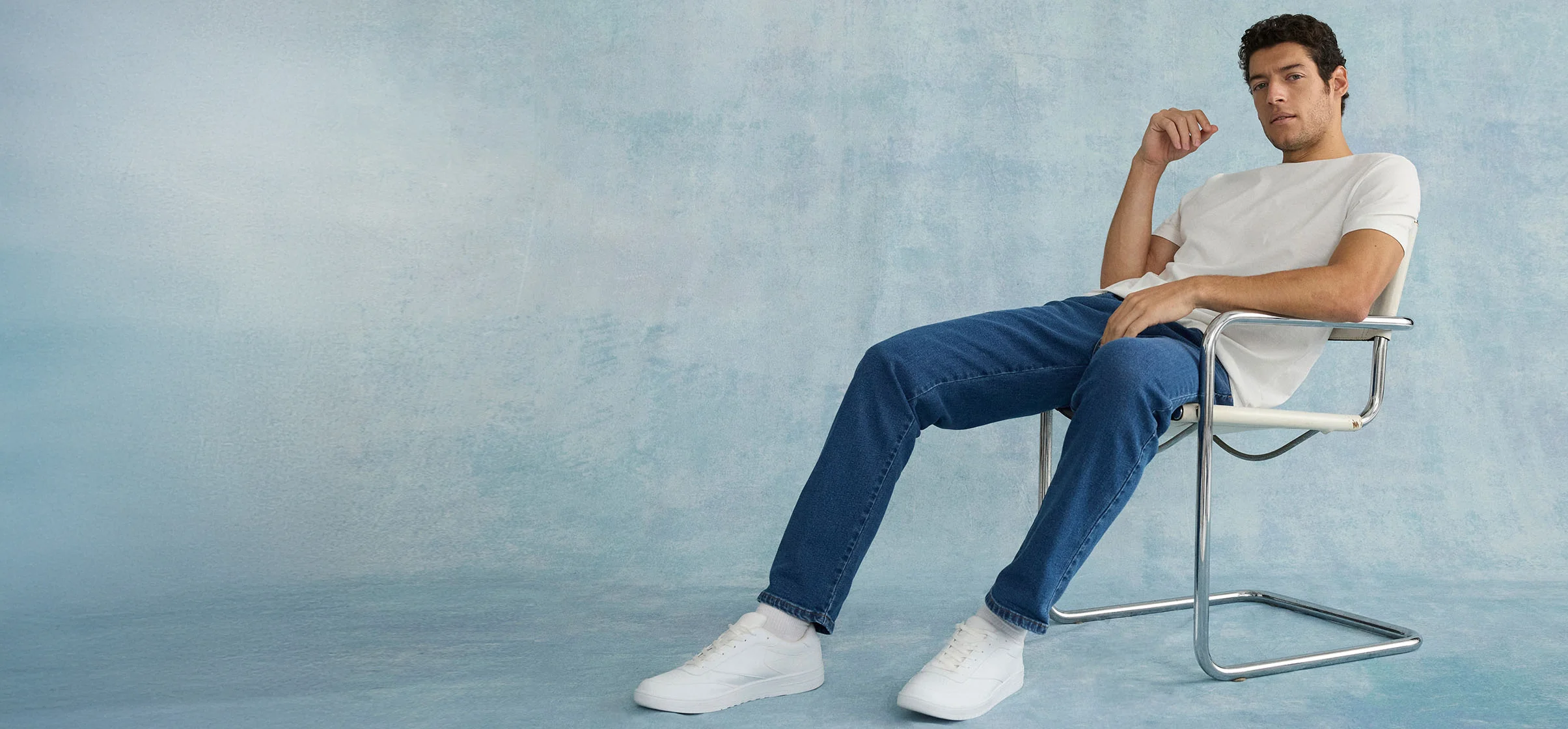 Casual look: wit T-shirt, blauwe jeans en witte sneakers op moderne stoel.