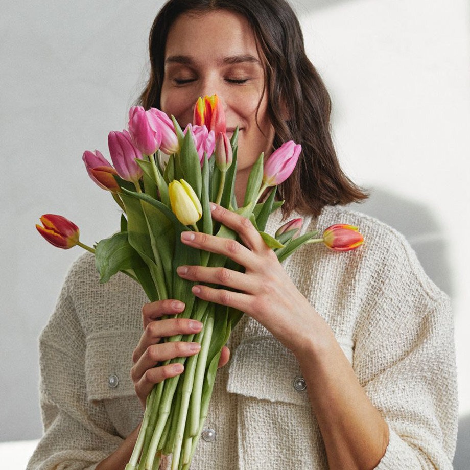 Persoon draagt witte, zachte trui en houdt bonte tulpen vast.