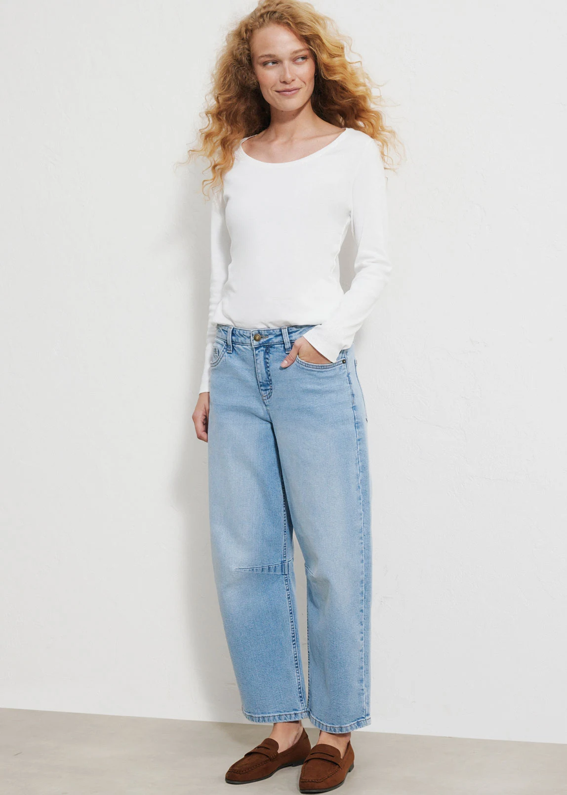 "Donkerblauwe barrel‑jeans met een hoge taille en licht afgeronde, taps toelopende pijpen, gemaakt van glad denim, gecombineerd met een wit T‑shirt en bruine schoenen."