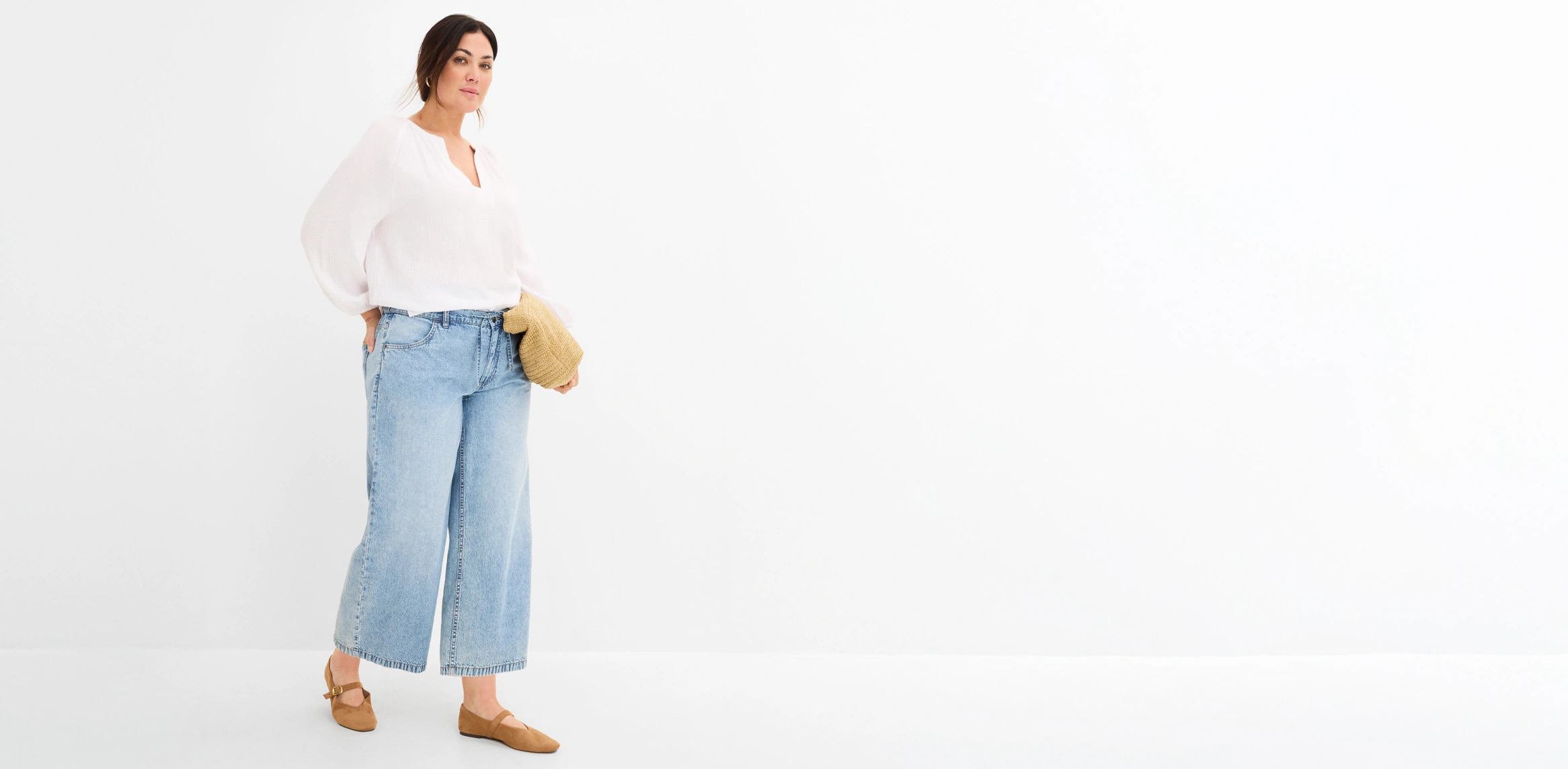 Outfit met een losse witte blouse, wijde jeans, bruine schoenen en een kleine gevlochten tas.