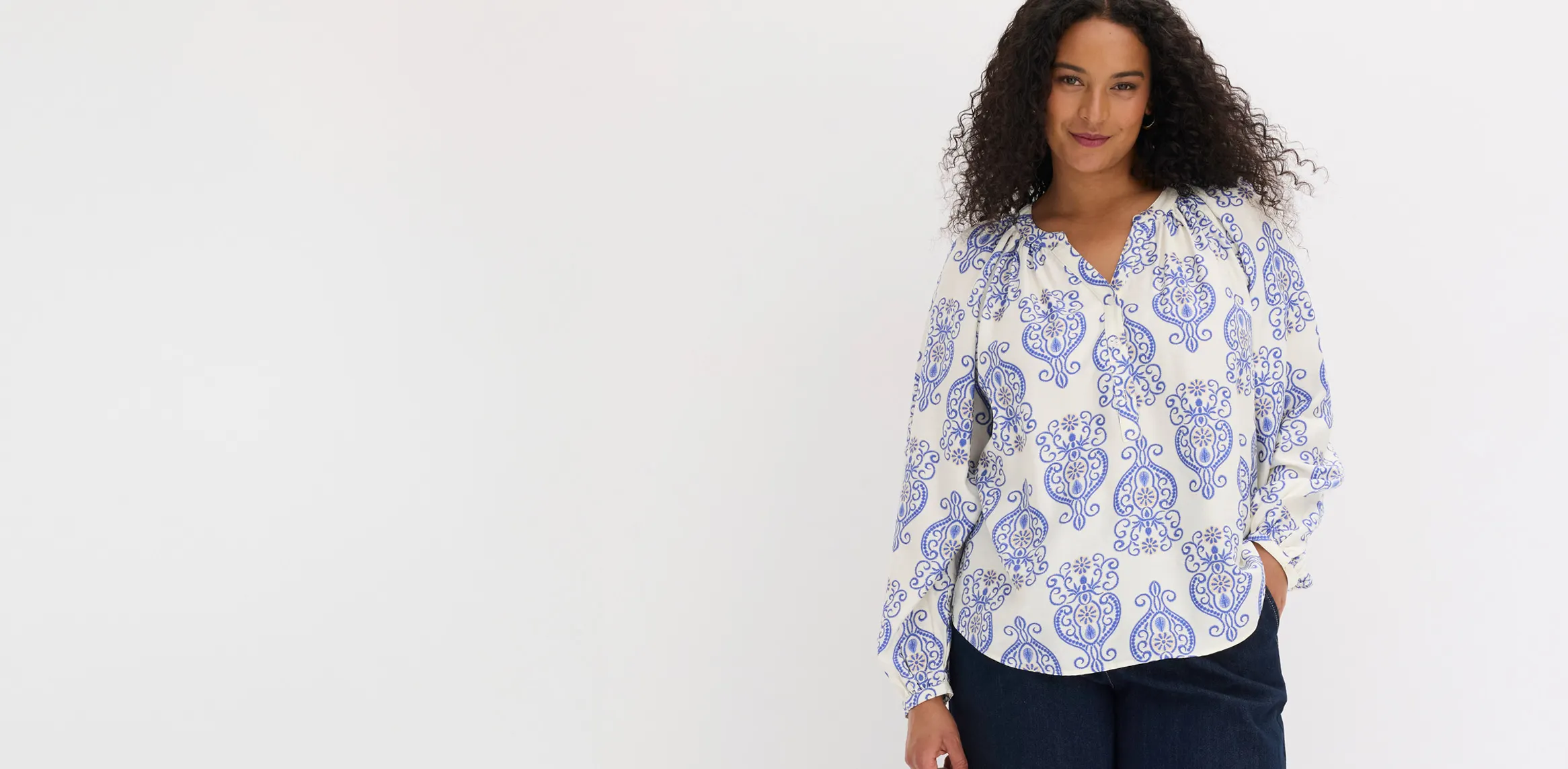 Witte blouse met lange mouwen, versierd met sierlijke blauwe motieven, gecombineerd met een donkere broek.