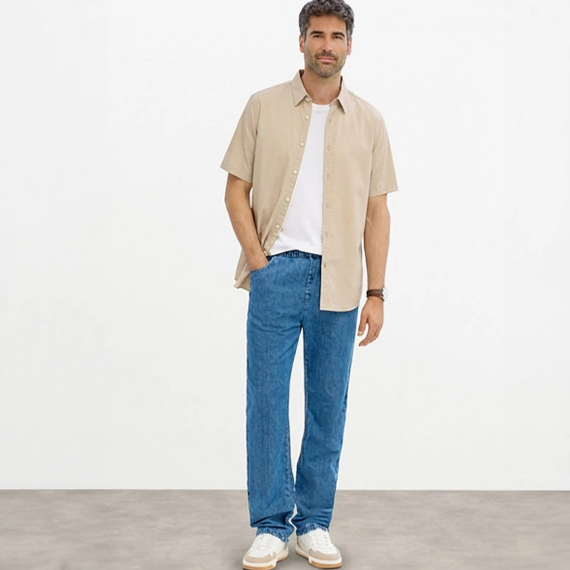 Beige overhemd met korte mouwen, wit T-shirt, blauwe Classic Fit jeans en witte sneakers.