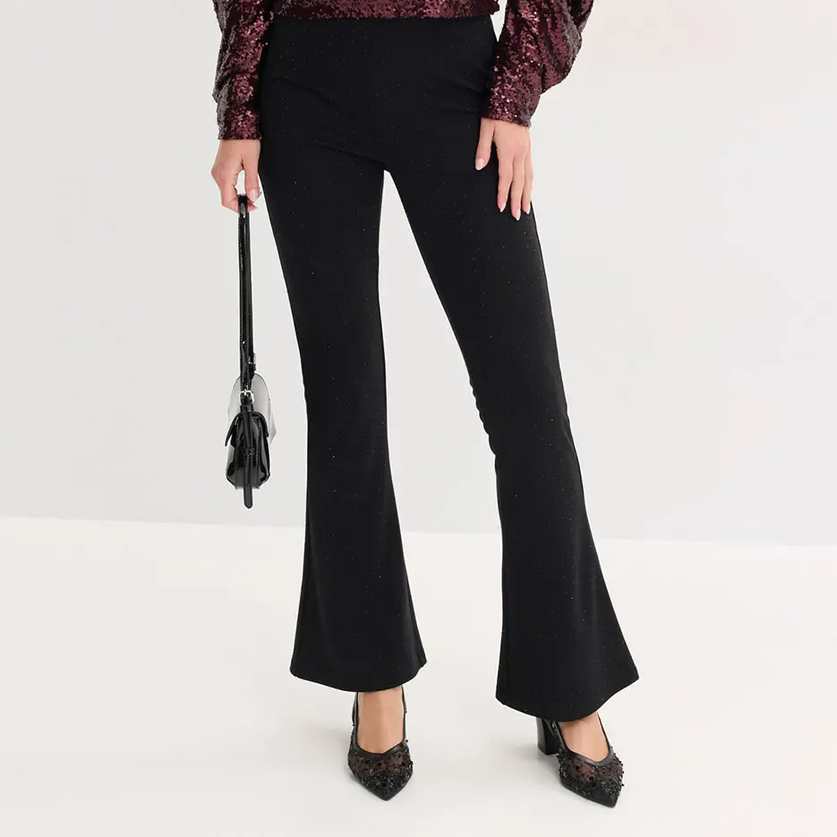 Elegante zwarte flared broek gecombineerd met blouse met pailletten en pumps met spitse neus.