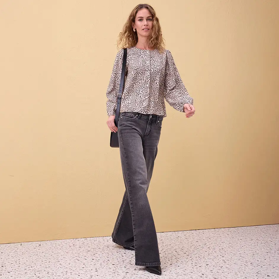 Luchtige gedessineerde blouse met pofmouwen, gecombineerd met grijze jeans met uitlopende pijpen.