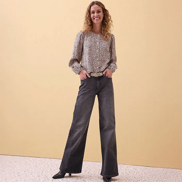 Luchtige gedessineerde blouse met pofmouwen, gecombineerd met grijze jeans met uitlopende pijpen.