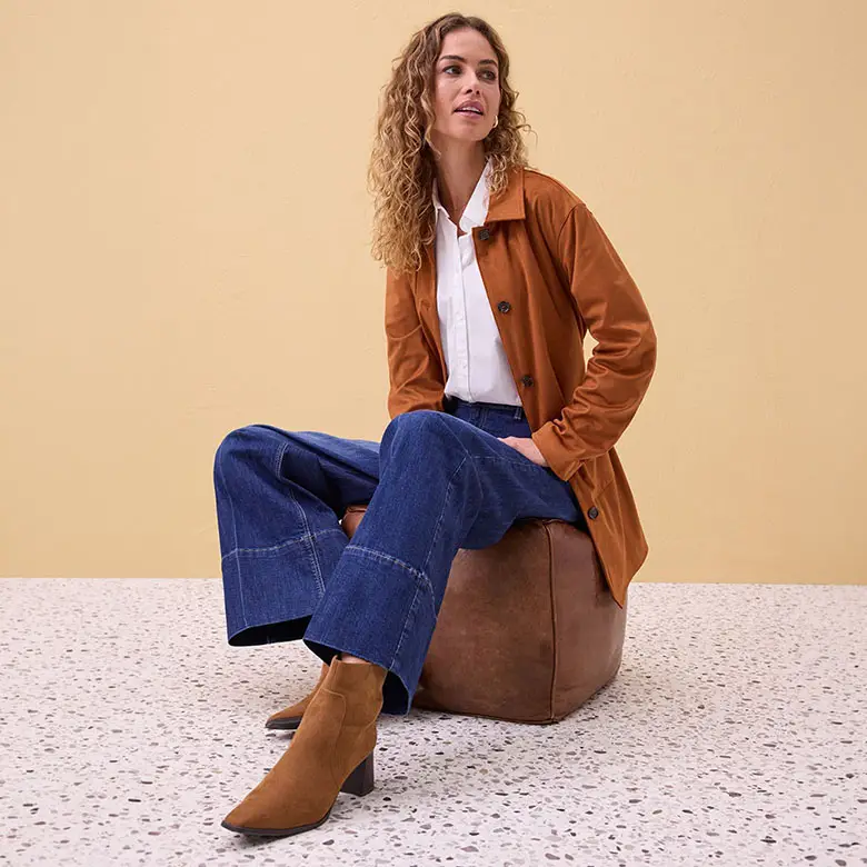 Lange cognackleurige jas, witte blouse, wijde jeans en bruine enkellaarsjes.