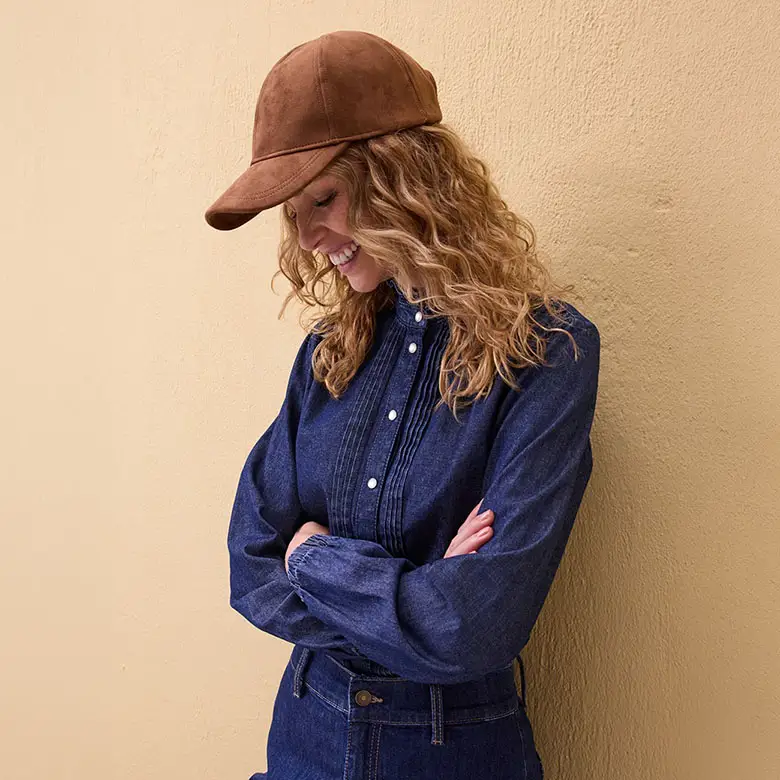 Blauwe spijkerblouse met knopen en bruine pet op krullend haar.