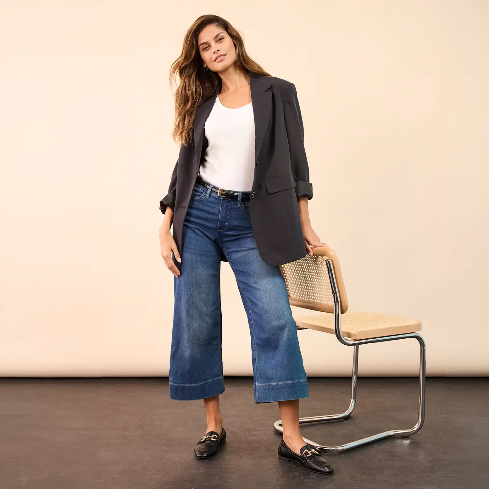 Elegante grijze blazer gecombineerd met witte top, wijde jeans en zwarte loafers.