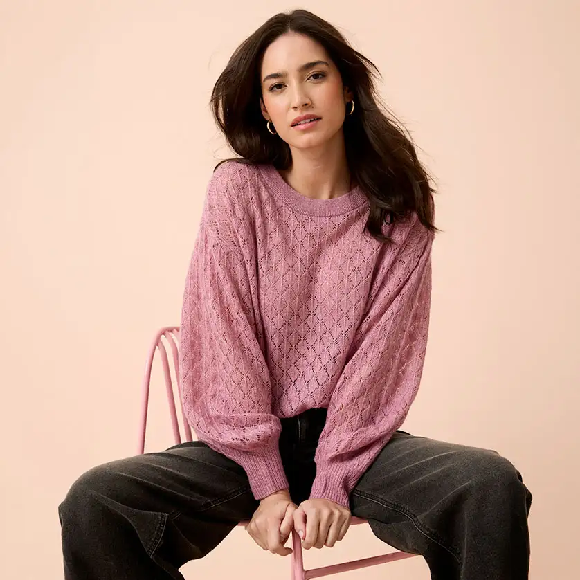 Zacht roze vest met kabelpatroon gecombineerd met donkere, wijde jeans.