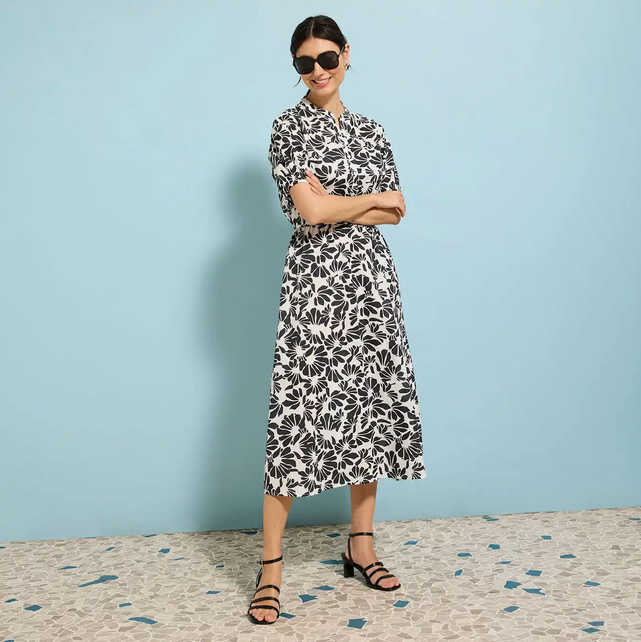Zomerse midi jurk met bloemenprint in zwart-wit, zonnebril en platte sandalen voor een elegante look.