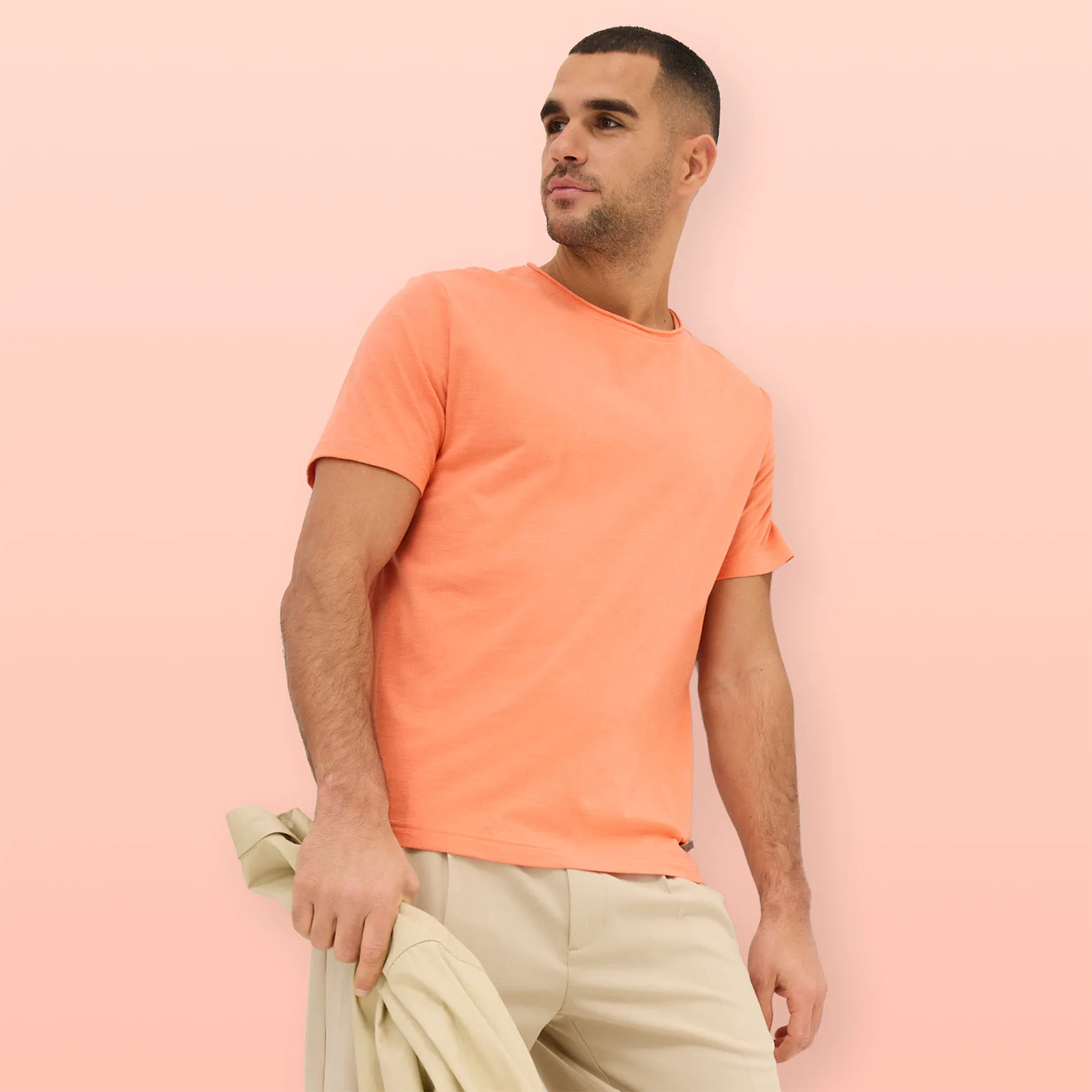 Perzikkleurig T-shirt gecombineerd met lichte broek en bijpassende trui als accessoire.