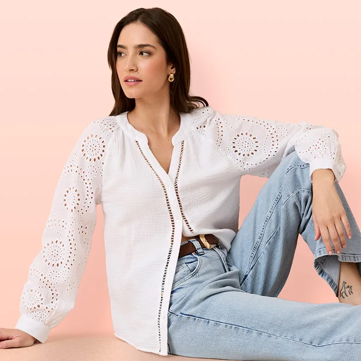 Witte blouse met gaatjesborduursel en lange mouwen gecombineerd met lichtblauwe jeans met riem.