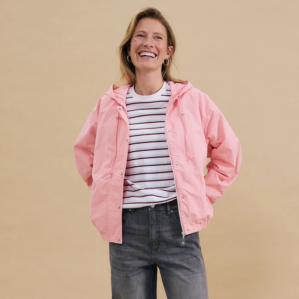 Roze jas over een gestreept shirt, gecombineerd met een grijze jeans – een casual vrijetijdslook.