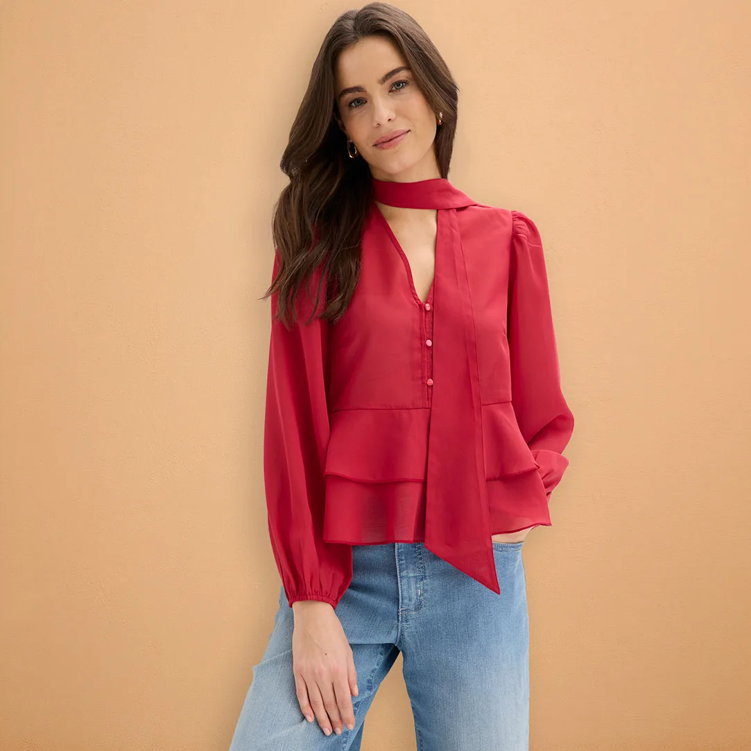 Een rode blouse met lange mouwen, gecombineerd met lichtblauwe jeans.