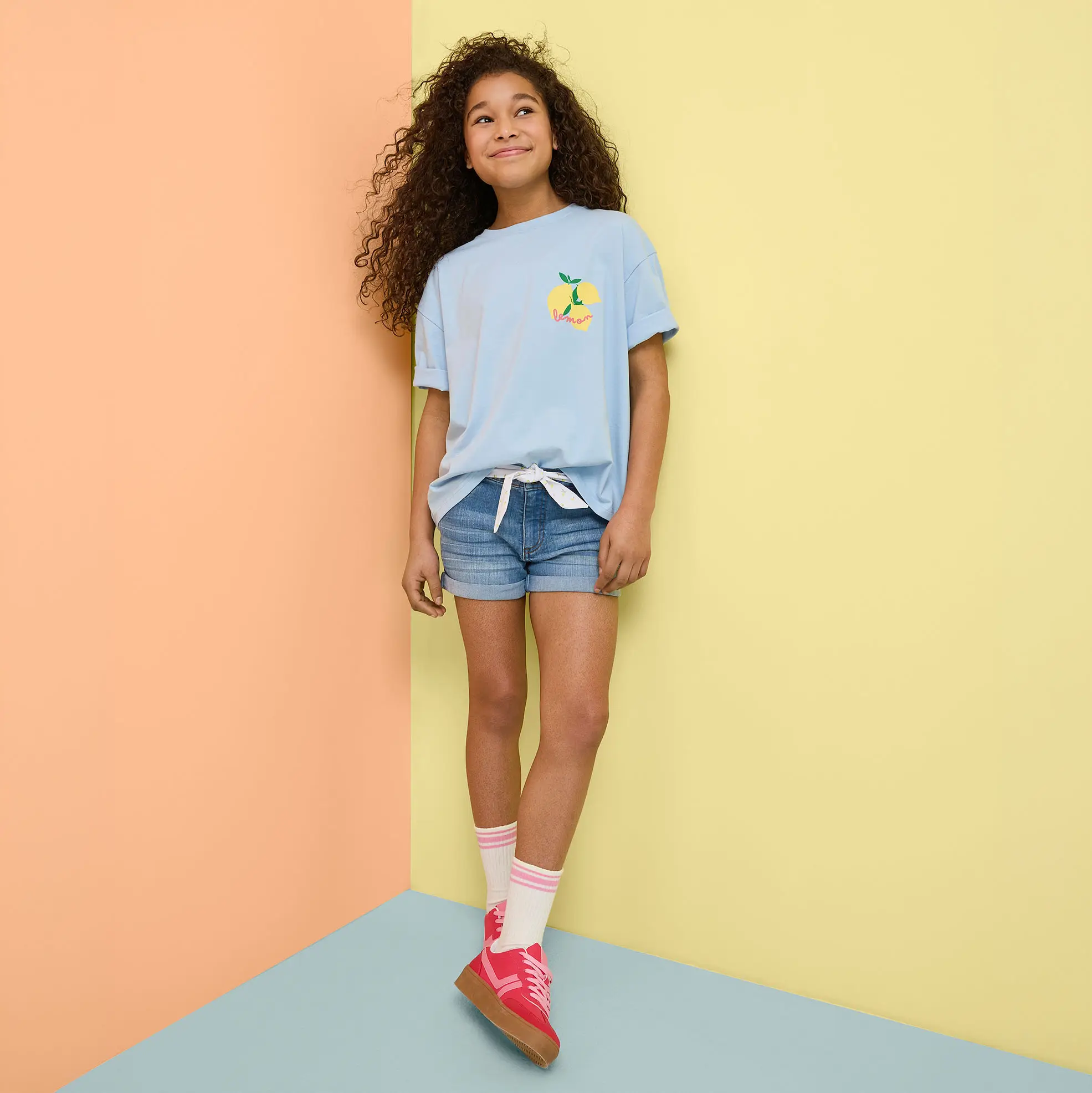 Zomeroutfit met lichtblauw T-shirt, jeans shorts en kleurrijke sneakers.