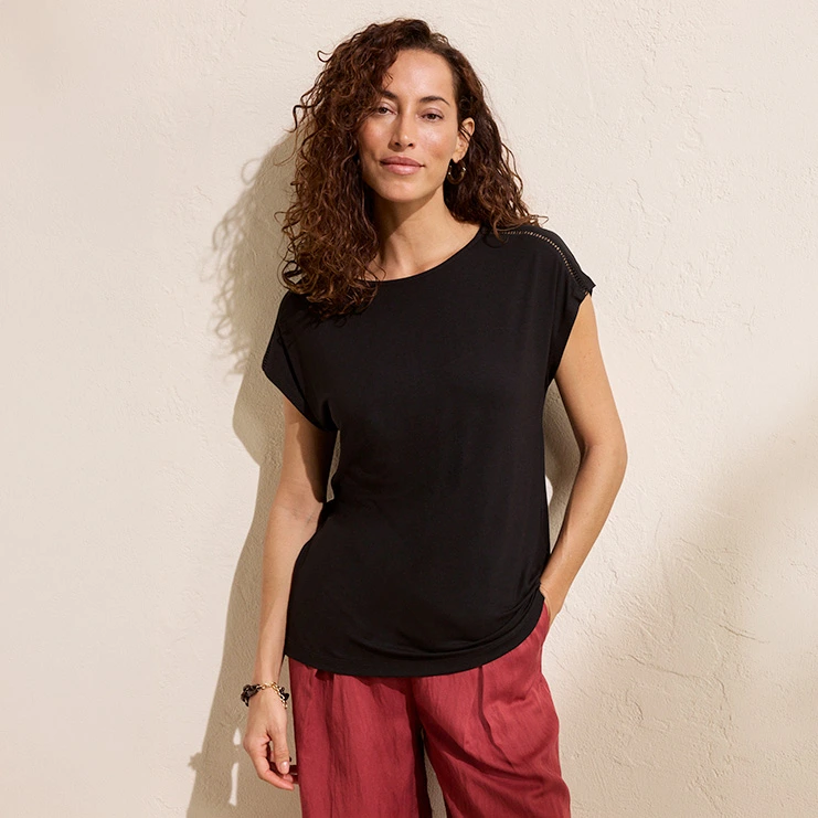 Vrouw draagt rode broek en zwart shirt met korte mouwen.