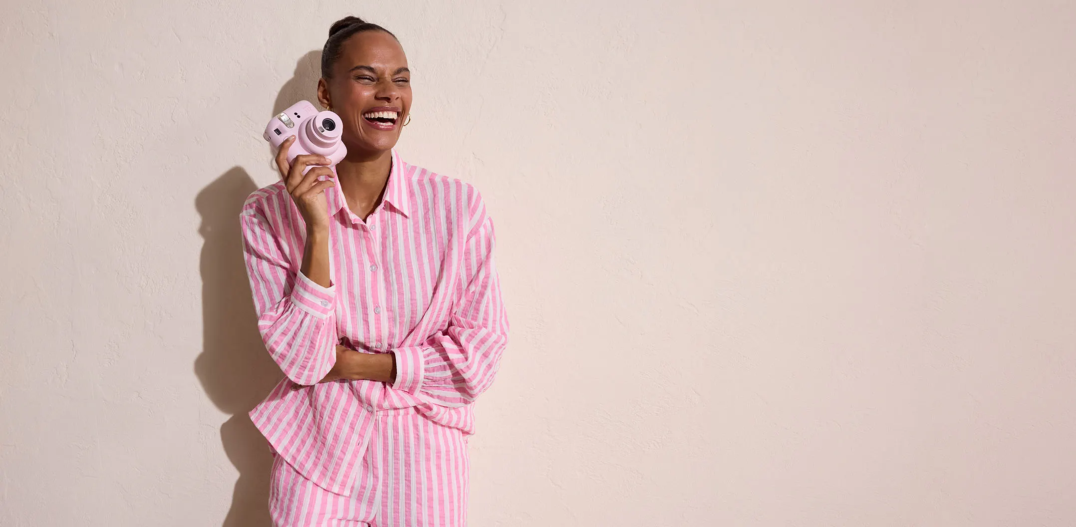 Vrouw draagt roze-wit gestreepte blouse en houdt een camera vast.