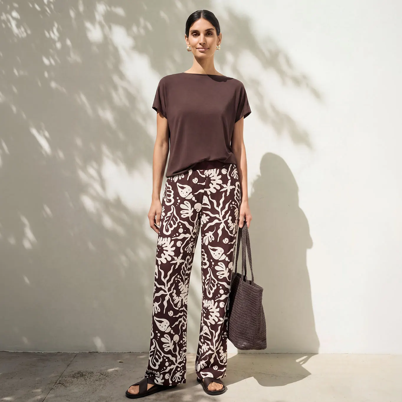 Basic bruin shirt en wijde broek met motief gecombineerd met donkere sandalen en tas.