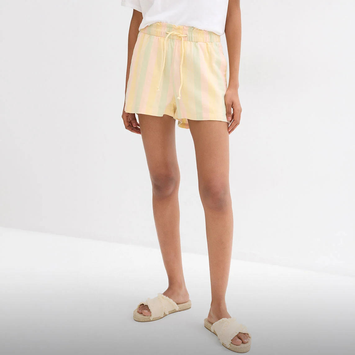 Gestreepte pastelkleurige short, wit T-shirt en comfortabele sandalen met raffialook voor warme dagen.