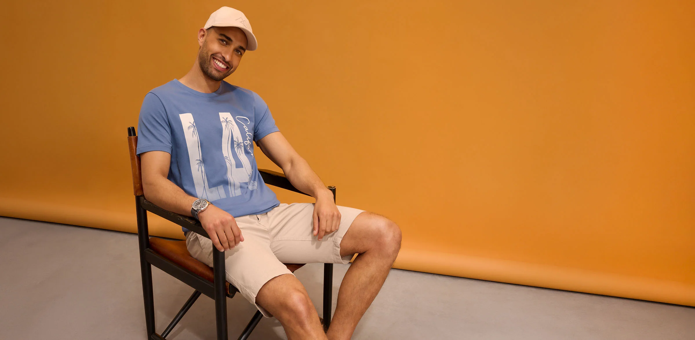 Casual look: pet, blauw T-shirt met print, beige short en polshorloge.