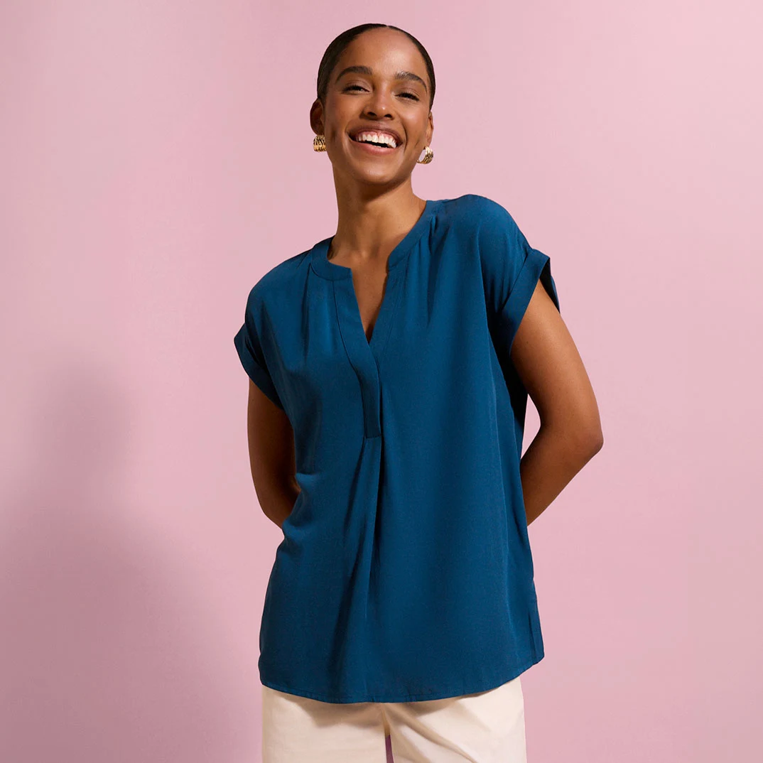 Modieuze tealkleurige blouse met V-hals en opgerolde mouwen, gecombineerd met lichte broek.