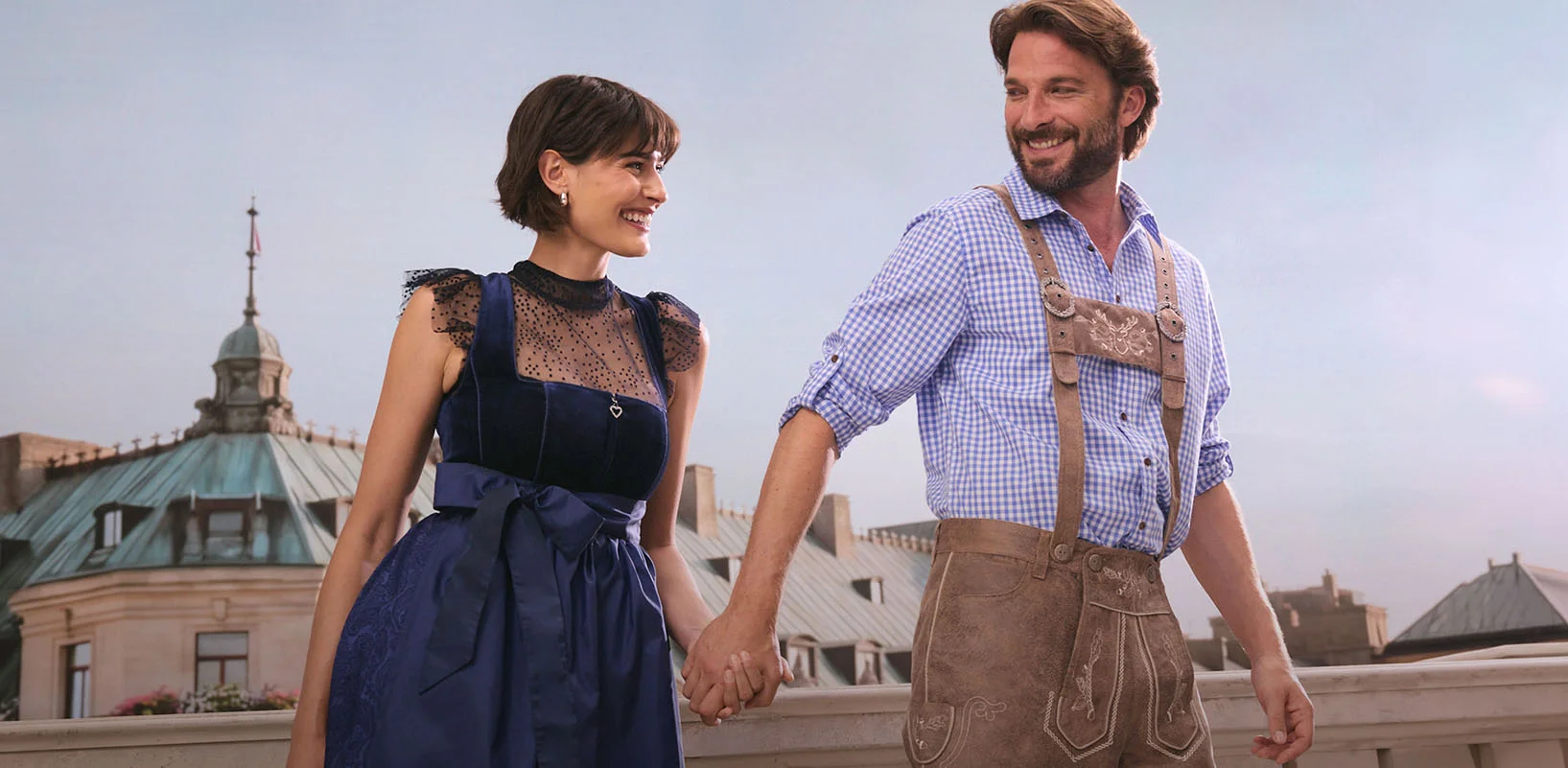 Zij draagt een elegante donkerblauwe dirndl, hij een klassieke Tiroler bermuda en een geruit overhemd.