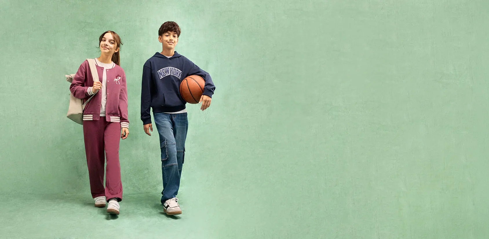 Meisje in trainingspak en bomberjack, jongen in New York-hoodie en cargo jeans.
