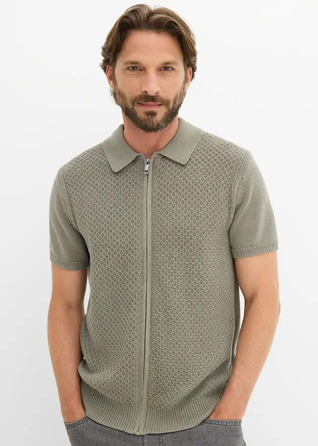 Gebreid groen poloshirt met ritssluiting en opvallend motief, gecombineerd met donkere jeans.