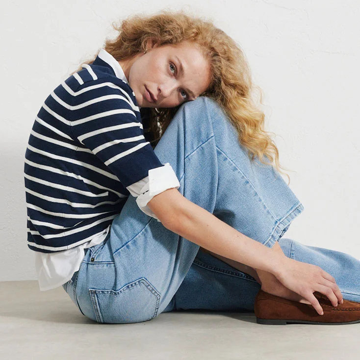 Gestreepte trui over een wit overhemd, wijde blauwe jeans en bruine loafers.