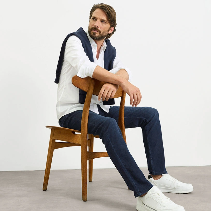 Stijlvolle casual look: wit overhemd, blauwe trui, jeans  en witte sneakers.