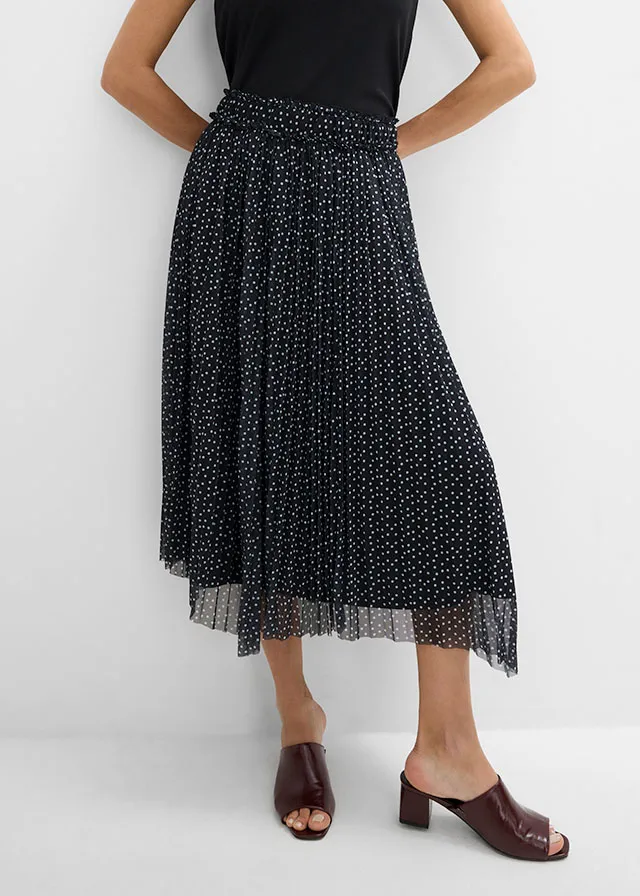 Basic zwarte top, gestippelde plissé rok en elegante donkerbruine instappers.
