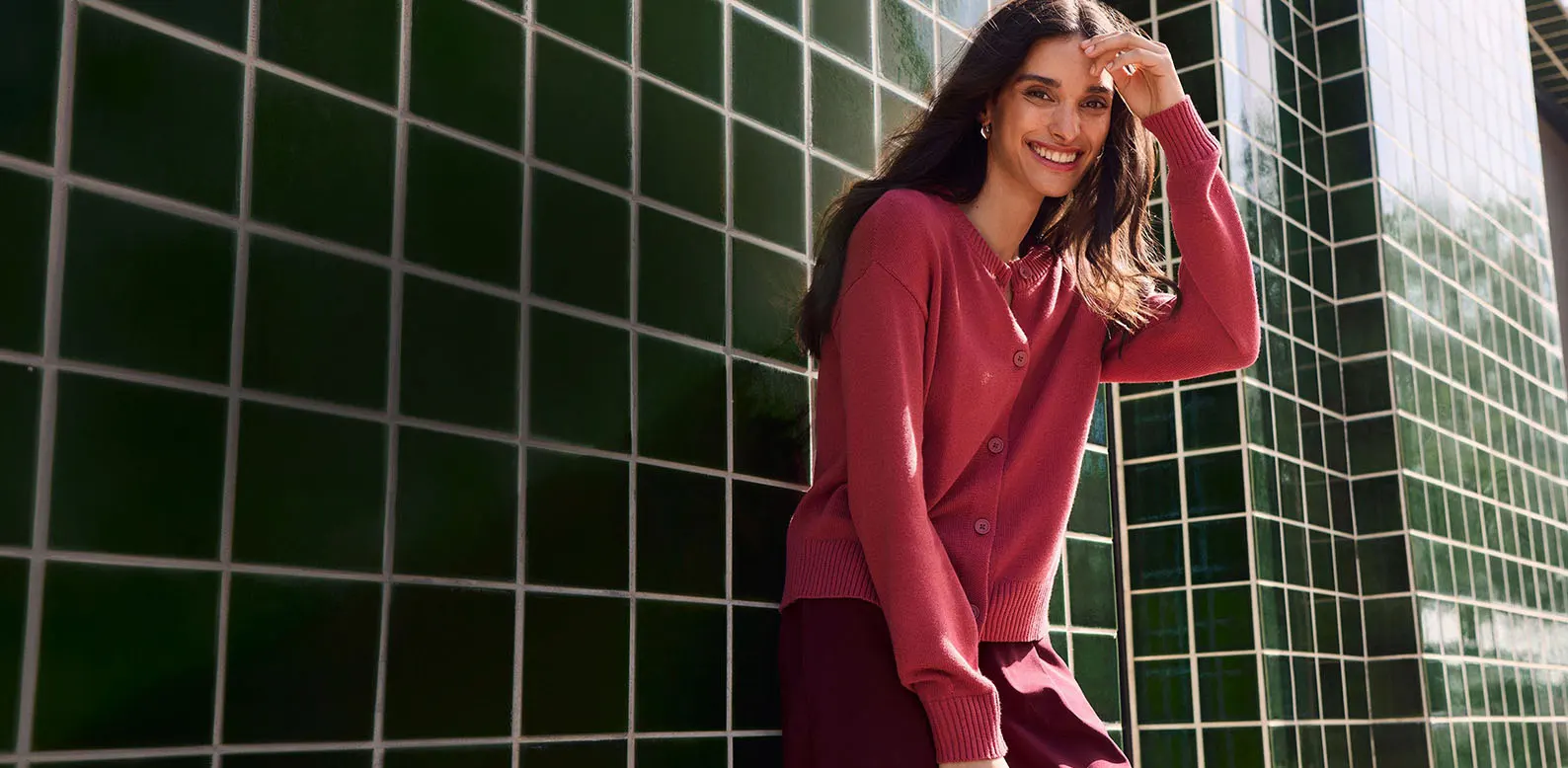 Vrouw draagt roze gebreid vest en wijnrode wijde broek.