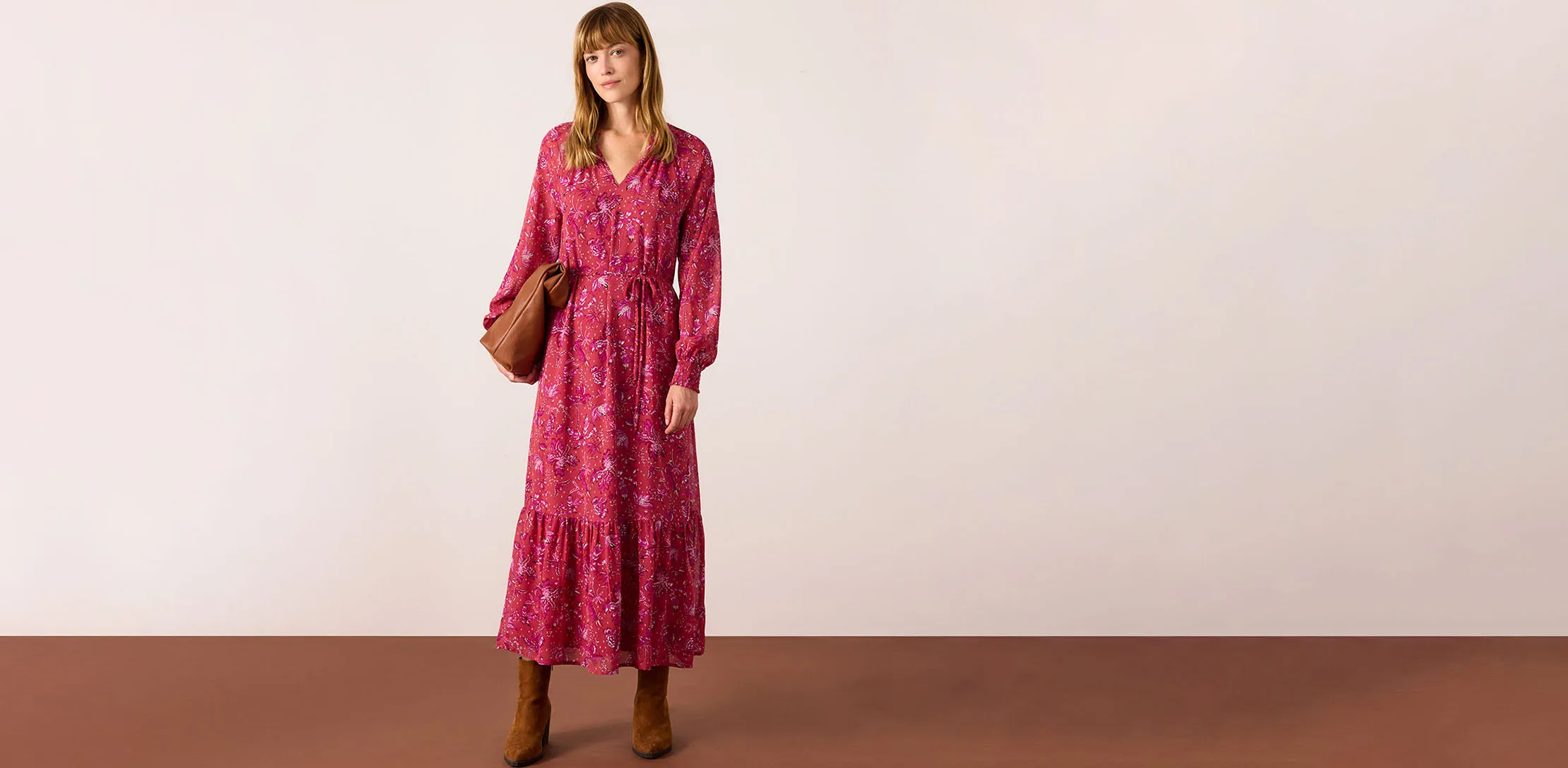 Rode maxi jurk met bloemenprint gecombineerd met bruine laarzen en handtas.