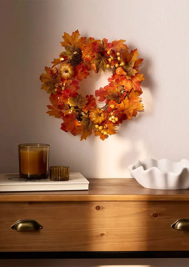 Een verlichte herfstkrans siert de muur. Op de houten tafel staan kaarsen en een schaal.