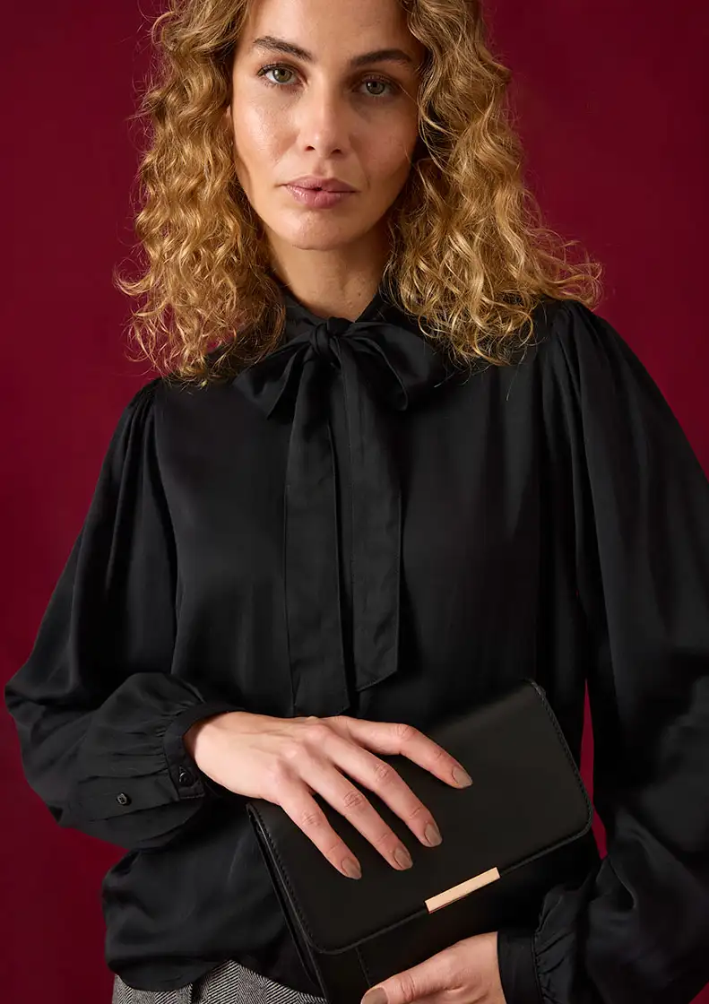 Zwarte blouse met elegante strik en wijde mouwen, gecombineerd met elegante clutch.