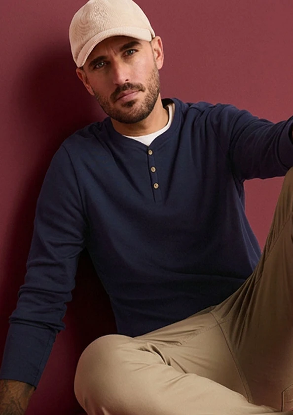Man draagt beige pet, marineblauw Henley shirt en beige broek.