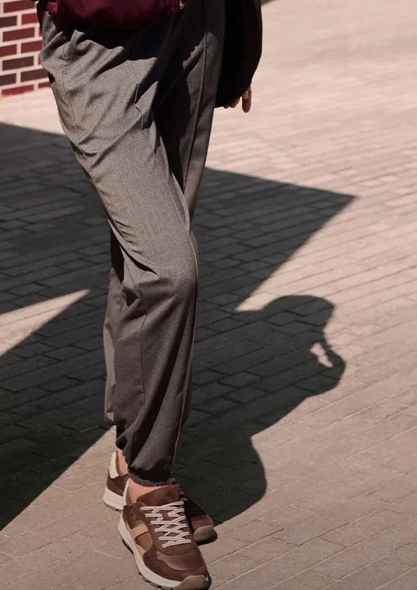 Grijze stoffen broek en bruine sneakers zetten bij deze casual-elegante look de toon.