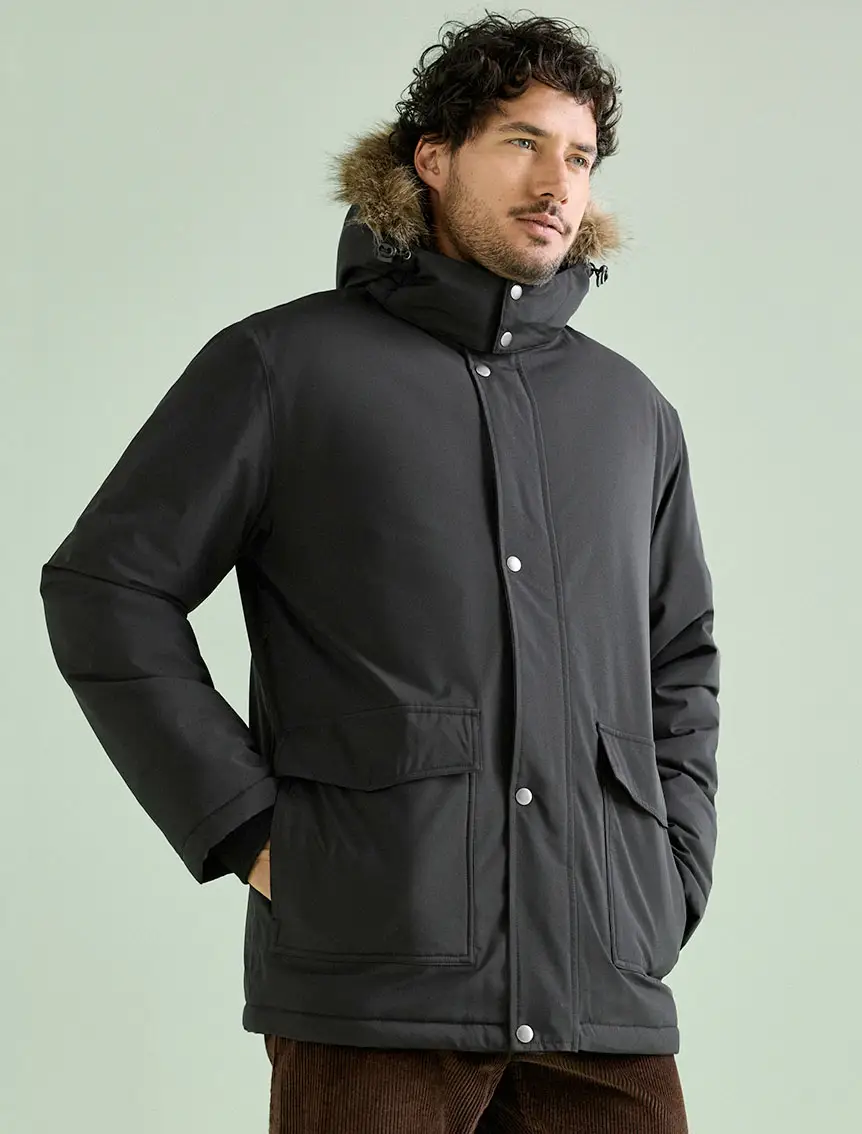 Deze man draagt een zwarte parka met capuchon met imitatiebont en een bruine corduroy broek.