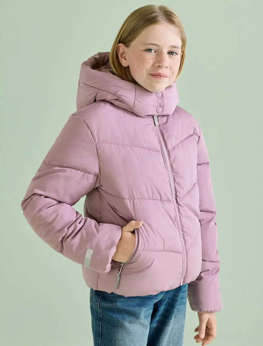 Dit meisje draagt een warme paarse gewatteerde jas met capuchon en een blauwe jeans.