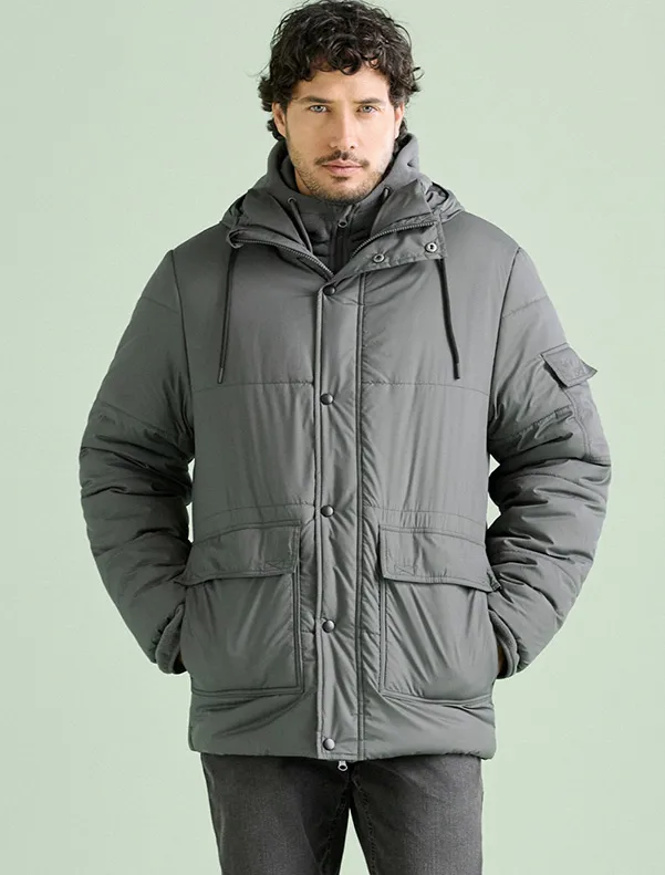 Deze man draagt een stylish grijze gewatteerde jas met capuchon en handige zakken.