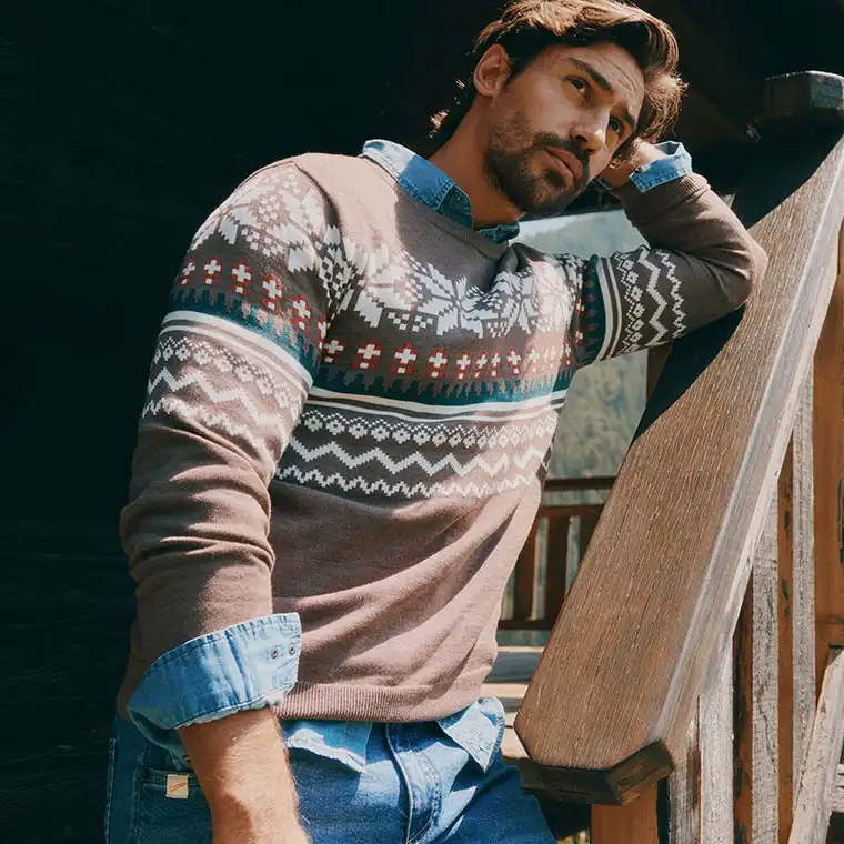 Deze man draagt een trui met motief over een spijkeroverhemd met een blauwe jeans eronder.