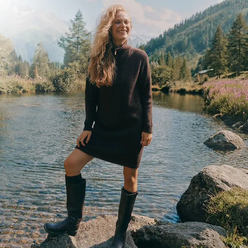 Deze vrouw draagt een donkere gebreide jurk met ritssluiting en hoge, donkere laarzen.