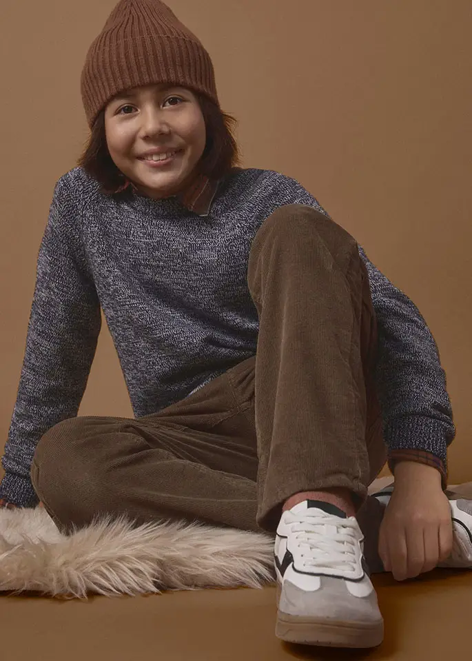 Jongen in een warme trui, een ribfluwelen broek, een muts en sneakers.