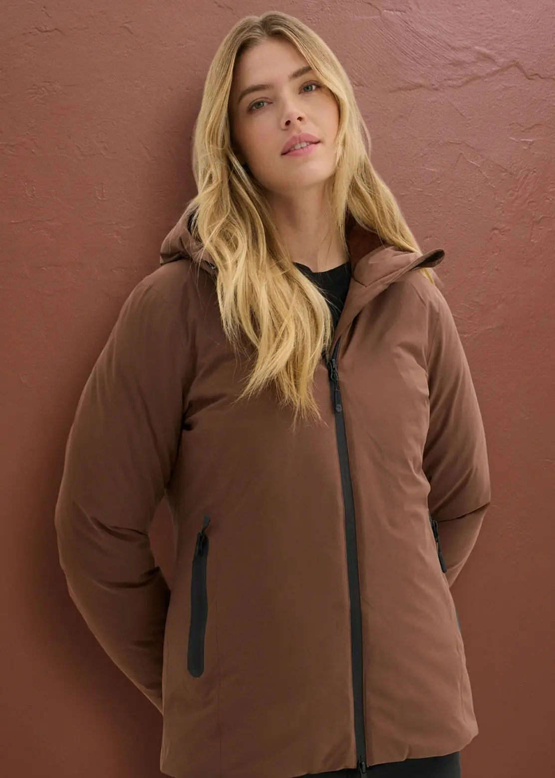 Deze vrouw draagt een stylish bruin gewatteerde jas met capuchon en zwarte ritssluitingen.